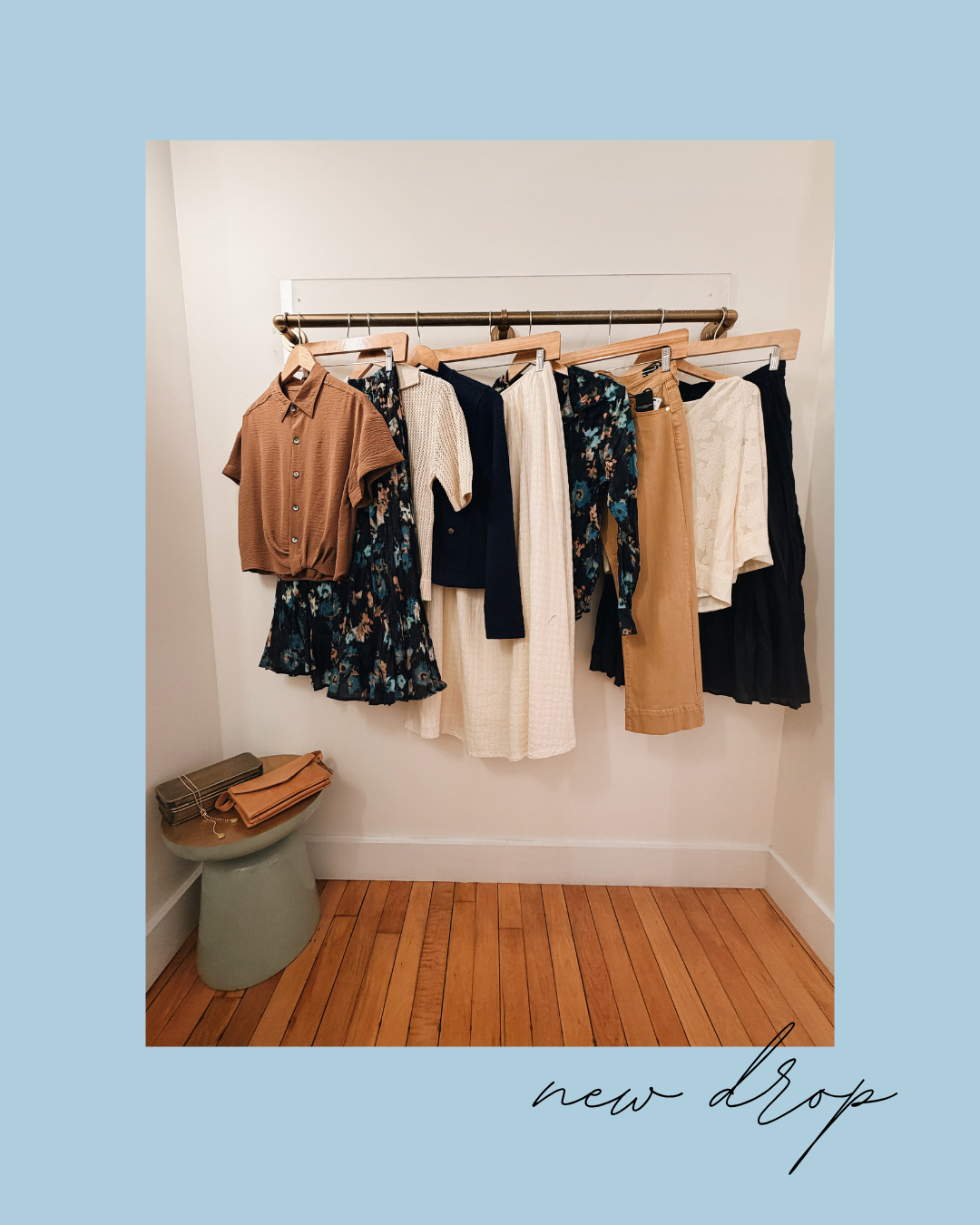Clothing rack with various garments against a white wall on a wooden floor, with 'new drop' text at the bottom.