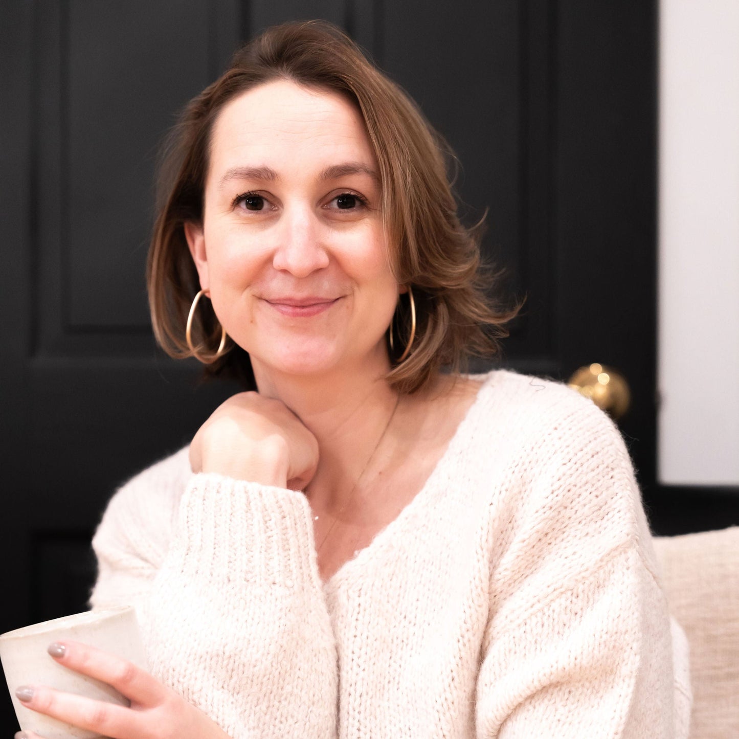 Headshot of Sarah DeFelice, owner of Bailey Road, wearing a soft, white sweater and holding a cup of tea in her hand.